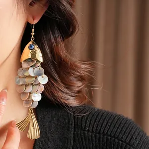 Vintage gold fish earrings with shell scales and evil eye charm on a fashion model
