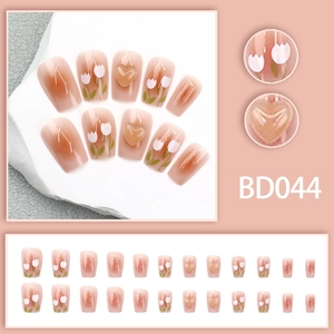 Detail of pink gradient press-on nails with white tulip art and 3D amber heart accents