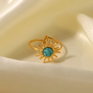 Detail of sun-shaped gold ring with turquoise inlay on elegant beige silk fabric