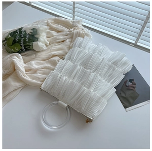 Close-up of white ruffled pleat handbag featuring a round clear acrylic handle and gold hardware