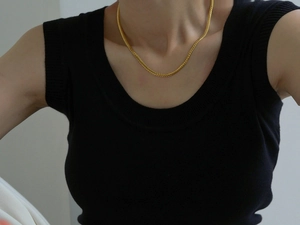 Close-up of minimalist gold snake chain necklace worn on neck over black clothing