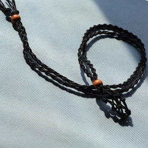 Detail of black hand-woven necklace cord with wooden beads and textured braiding