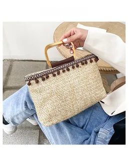 Close-up of beige woven straw bag with gold metal handle and brown leather grip
