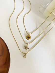 Detail of layered gold necklaces with starfish, sunburst, and floral charms on a tray