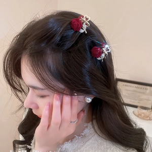 Detail of red rose hair claw clip with silver rhinestones worn by a model in soft light
