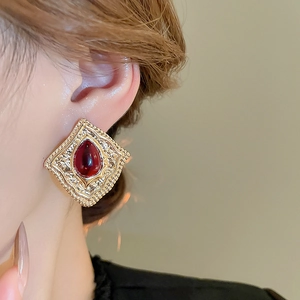Close-up of vintage golden rhombus earrings with red teardrop gemstone on a model