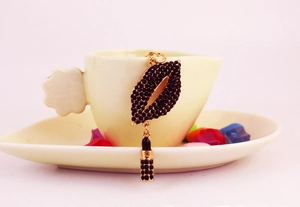 Detail view of a golden keychain with red lips and lipstick charms set with black crystals