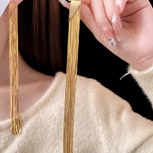 Detail of long gold tassel earrings with geometric triangle and hanging metal chains