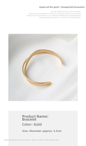 Dettaglio del bracciale rigido incrociato dorato con misure su sfondo di tessuto bianco