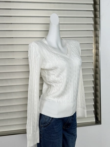 Detailed view of white V-neck cable knit sweater with ribbed cuffs and textured patterns