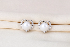 Macro detail of S925 silver heart pearl earrings with sparkling zircon on pink silk