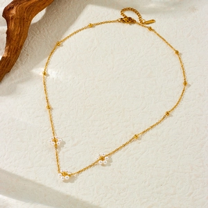 Collier artisanal en chaîne dorée avec fleurs de perles sur fond texturé naturel