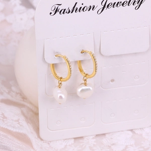 Close-up of golden pearl drop earrings with zircon inlay on a white lace background