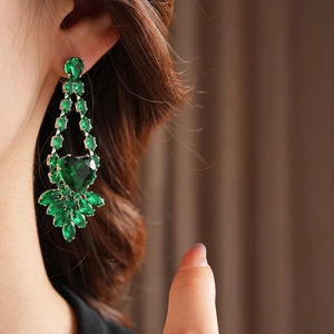 Detailed close-up of emerald heart earrings with leaf patterns on a model's ear