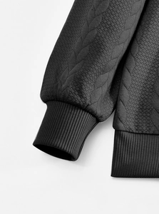 Detail of heavy knit fabric with textured diamond pattern and ribbed cuffs on black hoodie