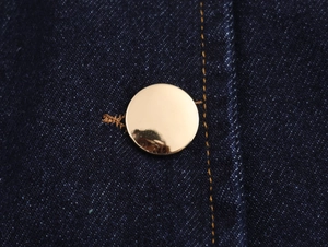 Gros plan d'un bouton doré sur gilet en jean bleu foncé avec coutures jaunes précises