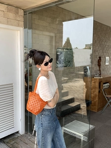 Close-up of vibrant orange hand-woven bucket bag styled with casual summer street outfit