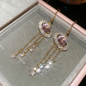 Detail of gold tassel earrings with pink oval crystal and sparkling star pendants