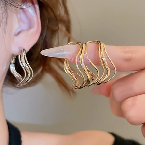 Close-up of irregular wave metal earrings in silver and gold on model's ear and hand