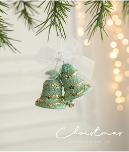 Green and gold Christmas bell ornament with white organza bow hanging on pine branch