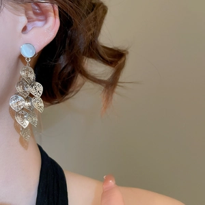 Close-up of dangling silver leaf earrings with white opal stone on a model