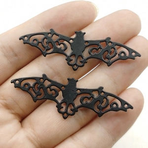 Pair of black hollow bat metal pendants for DIY jewelry making on a palm