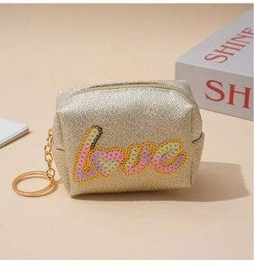 Detail view of a gold glitter coin purse featuring colorful LOVE sequin embroidery and a keychain