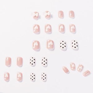Nude roze kunstnagels met zwarte stippen en witte 3D strikjes voor een manicure