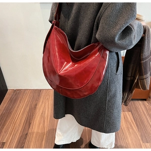 Detail of dark red half-moon shoulder bag with glossy PU leather finish on a gray coat