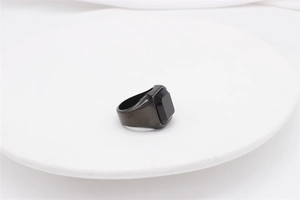 Macro shot of men's square black gemstone ring on white ceramic plate with brushed metal texture