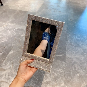 Detail of hand holding a foldable vanity mirror fully covered in sparkling silver rhinestones