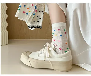 Detail of white mesh socks with colorful heart patterns worn with white canvas sneakers