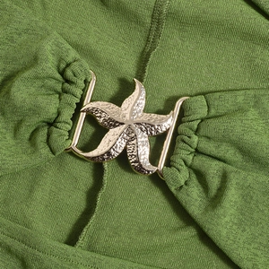 Detail of green knit dress featuring a gold starfish metal buckle ornament