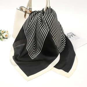 Close-up of elegant black and white striped silk scarf tied on a white leather handbag