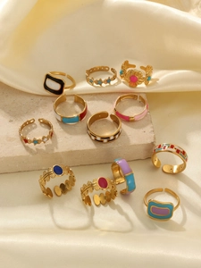 Detailed view of colorful enamel flower and geometric gold rings on beige silk fabric