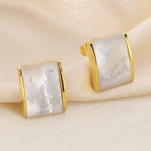 Macro shot of rectangular gold earrings with white mother-of-pearl inlays on satin cloth