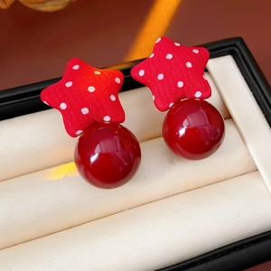 Macro shot of red polka dot star fabric earrings with glossy round pearls on beige velvet
