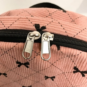 Detail of pink corduroy schoolbag with black bow pattern and silver double zippers