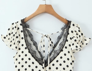 Detail of white polka dot dress featuring a V-neckline with black lace trim and ties