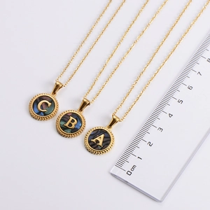 Detailed size measurement of golden initial shell pendants showing 1.5cm diameter on a ruler