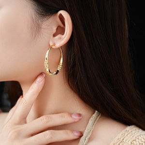Close-up of golden chunky hoop earring with textured stone finish worn by a model