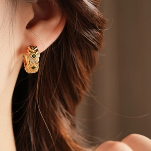 Macro view of vintage gold quilted earrings with emerald green and white zircon stones