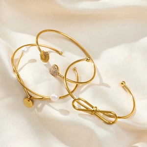 Detailed view of 18k gold plated bracelets with charms on beige silk fabric