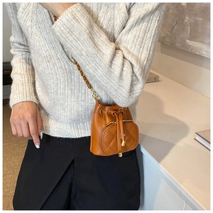 Brown mini bucket bag with chain strap and camellia drawstring detail on gray sweater