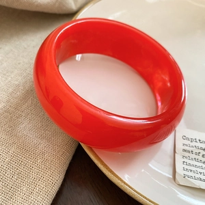 Detail of a glossy wide red resin bangle with a translucent finish and smooth texture