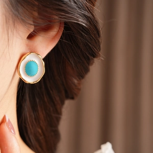 Close-up of vintage style gold-rimmed enamel earrings worn by a model in profile view