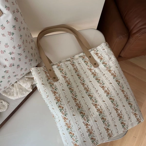 Détail du sac cabas floral montrant les anses en cuir marron et les rivets robustes