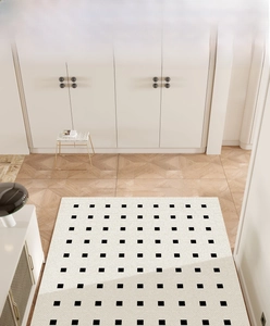 Detailed view of cream PVC doormat with black grid pattern on a light wood floor