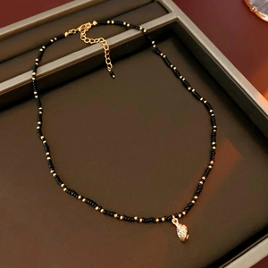 Detailed close-up of a black beaded necklace featuring a golden seashell pendant