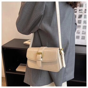 Modern beige leather crossbody bag worn with a gray suit in an elegant lifestyle setting